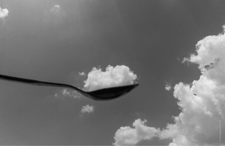 a black and white photo of a street light with clouds in the sky behind it