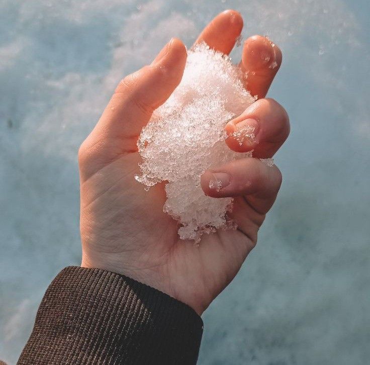 a person holding some type of white substance in their hand and ice on the water behind them