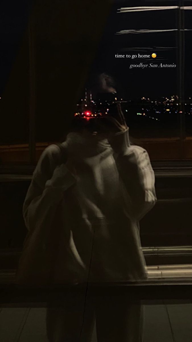 a person standing in front of a window at night talking on a cell phone and looking out the window