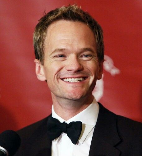 a man in a tuxedo smiles at the camera while speaking into a microphone