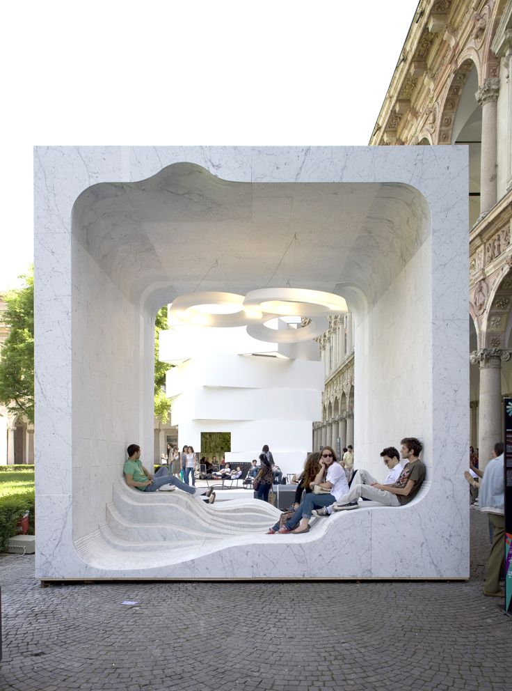 people sitting on benches in the middle of an open area with white walls and columns