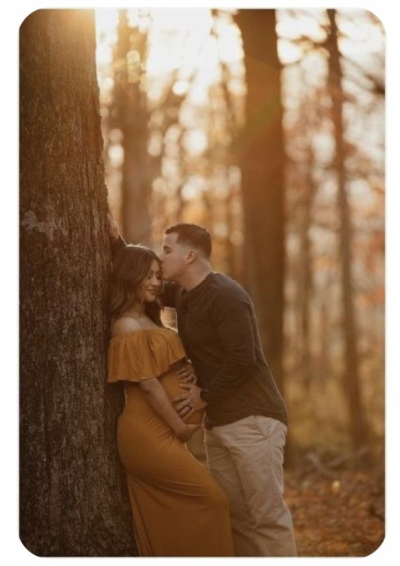 a couple cuddles against a tree in the woods at sunset during their engagement session