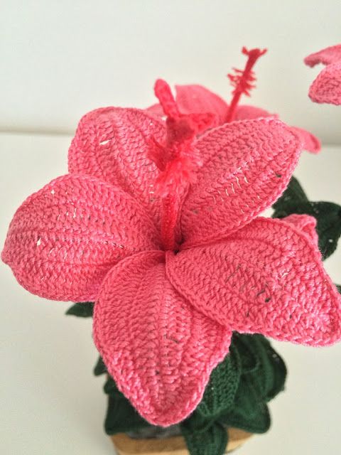 a crocheted pink flower sitting on top of a green plant