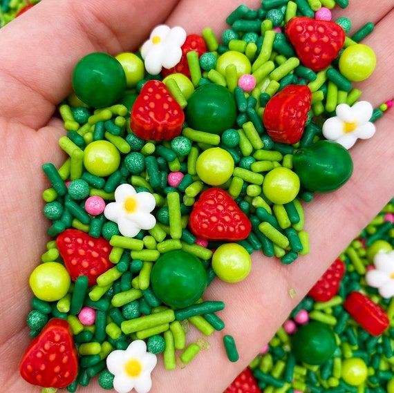 a hand is holding a small green and red bead with strawberries, flowers, and peas