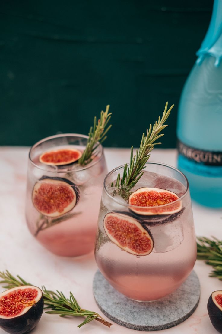 two glasses filled with pink wine and topped with fresh figs, rosemary sprigs and an olive branch