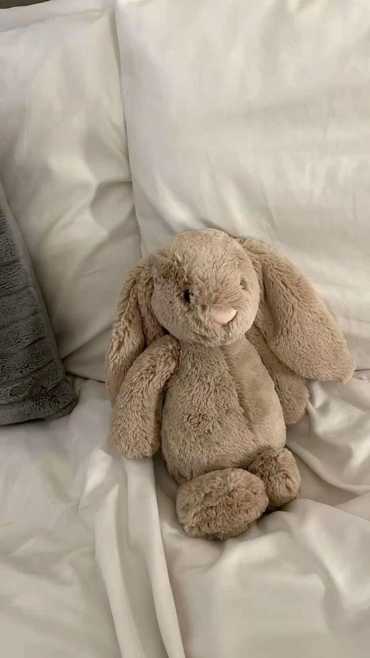 a stuffed rabbit sitting on top of a bed next to white sheets and pillows,