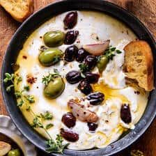 a bowl filled with olives, sour cream and bread on top of a wooden table