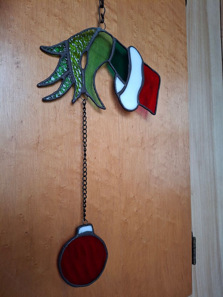 a decorative glass piece hanging from a chain on a wooden door with a hand holding a christmas ornament