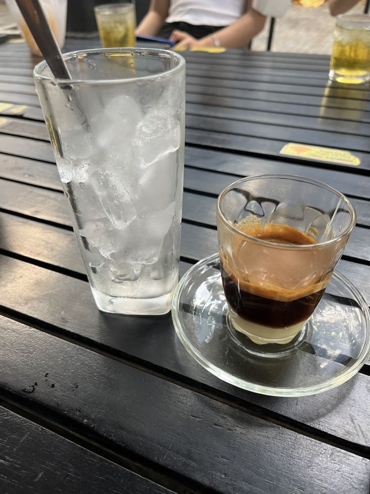 there is a cup of coffee on the table next to a glass with ice in it