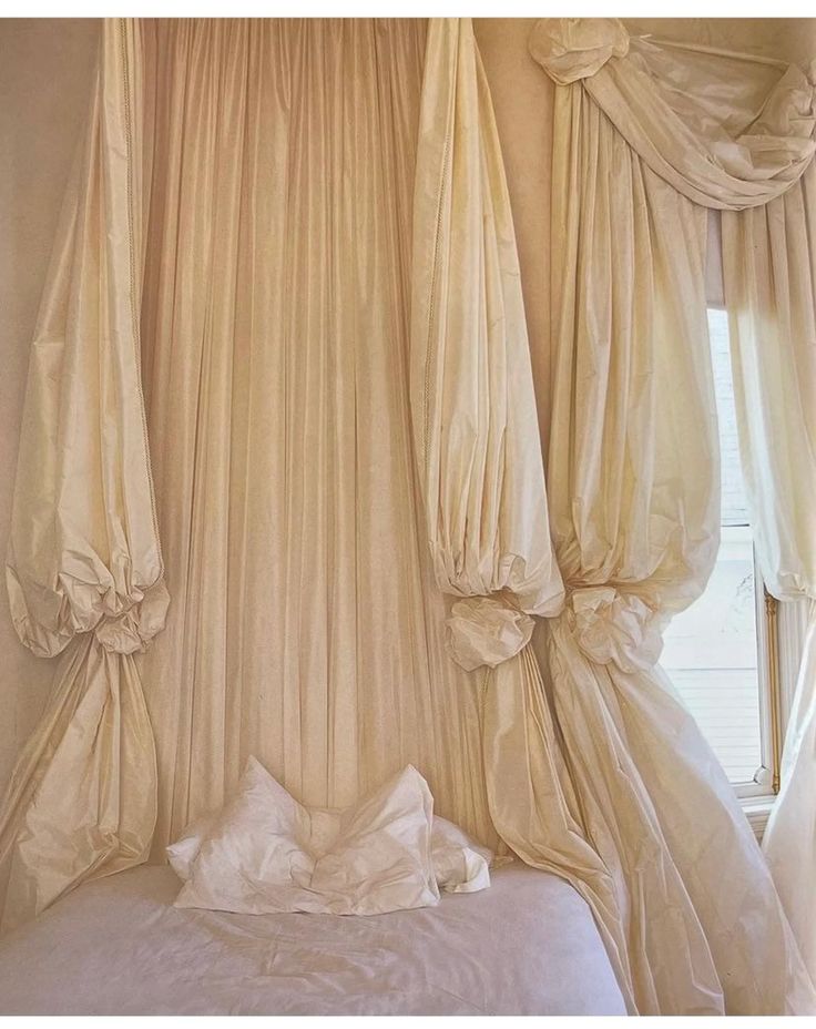 an unmade bed with drapes hanging from it's sides and pillows on the bottom