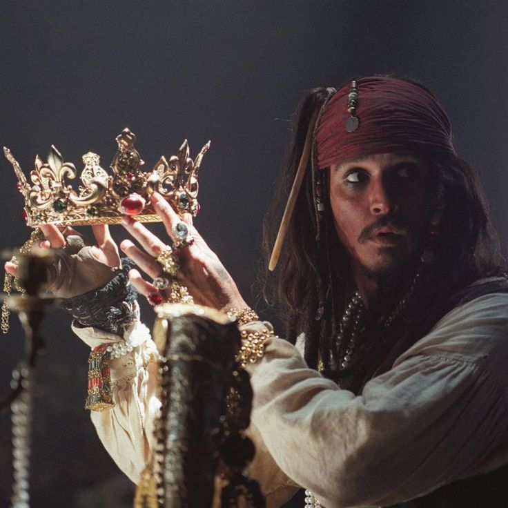 a man dressed in pirate costume holding up a golden crown on top of a table