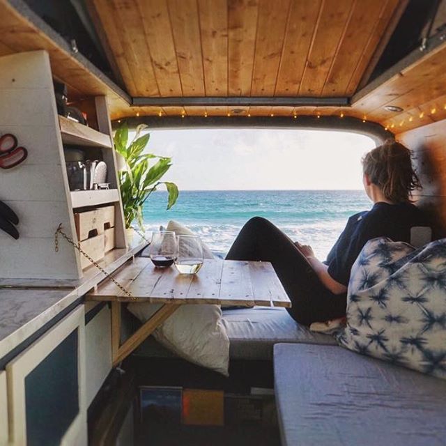 a woman sitting in the back of a camper van looking out at the ocean