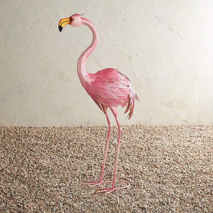 a pink flamingo standing on top of a pile of gravel next to a wall