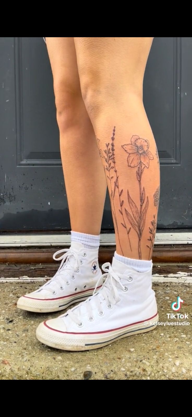 a woman's legs with tattoos on them and flowers in the bottom part of her leg