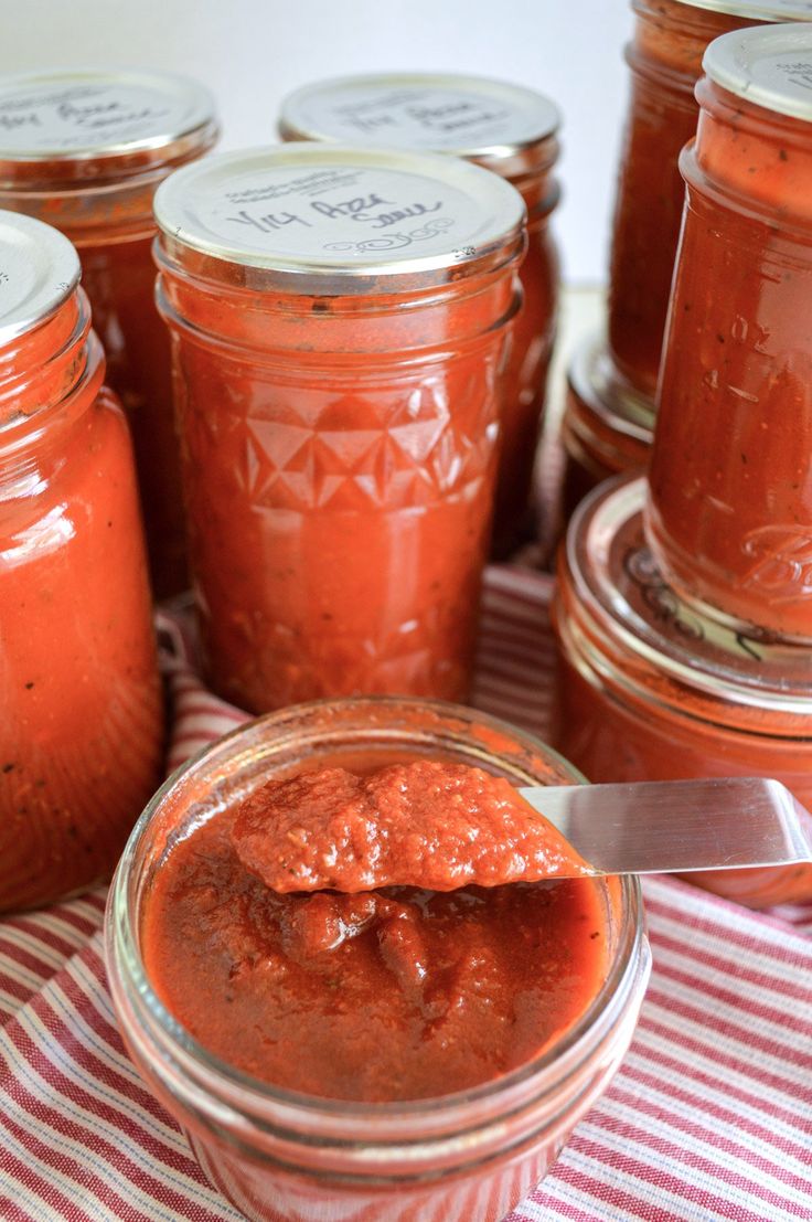 several jars filled with red sauce sitting on top of a checkered table cloth next to a knife