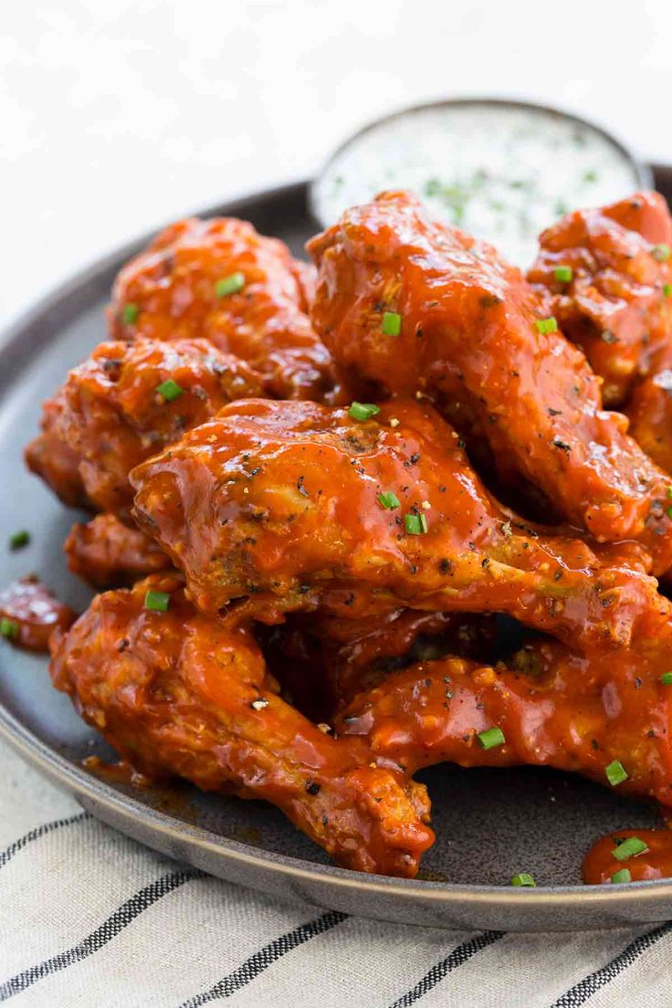 a plate full of chicken wings with sauce on the side and garnished with parsley