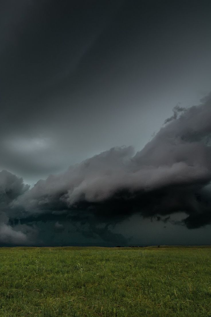 a large field with grass and storm clouds in the sky above it on an overcast day