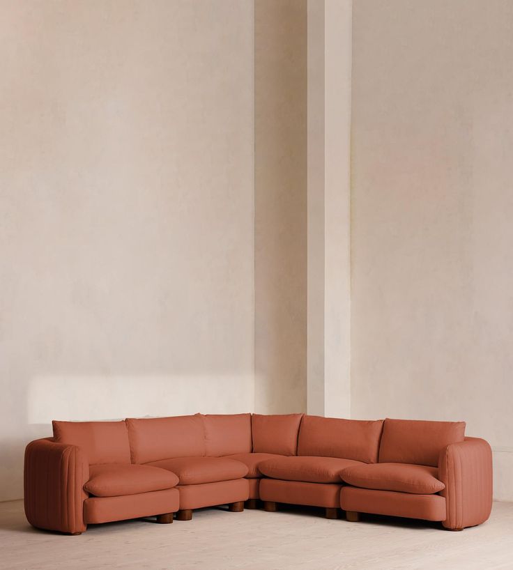 an orange leather sectional sofa sitting on top of a hard wood floor next to a white wall