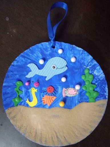 a paper plate with an image of a dolphin and fish on it, hanging from a blue ribbon