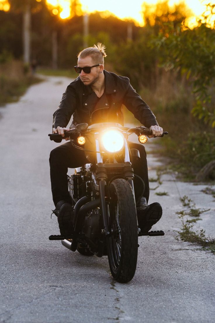 a man riding on the back of a motorcycle down a country road at sunset or dawn