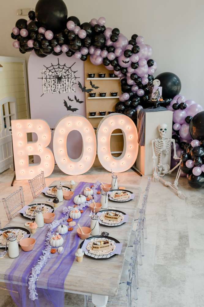 a table topped with lots of desserts next to a boo sign filled with balloons