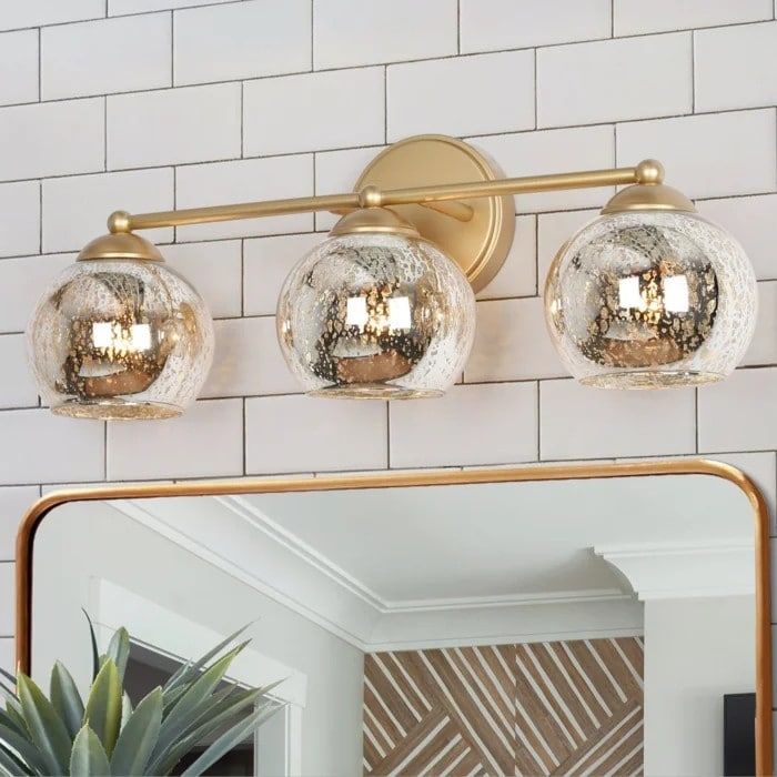 a bathroom vanity with three lights and a mirror on the wall next to a potted plant