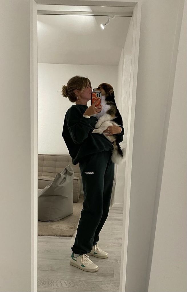 a woman taking a selfie with her dog in the mirror while she is wearing sweatpants and sneakers