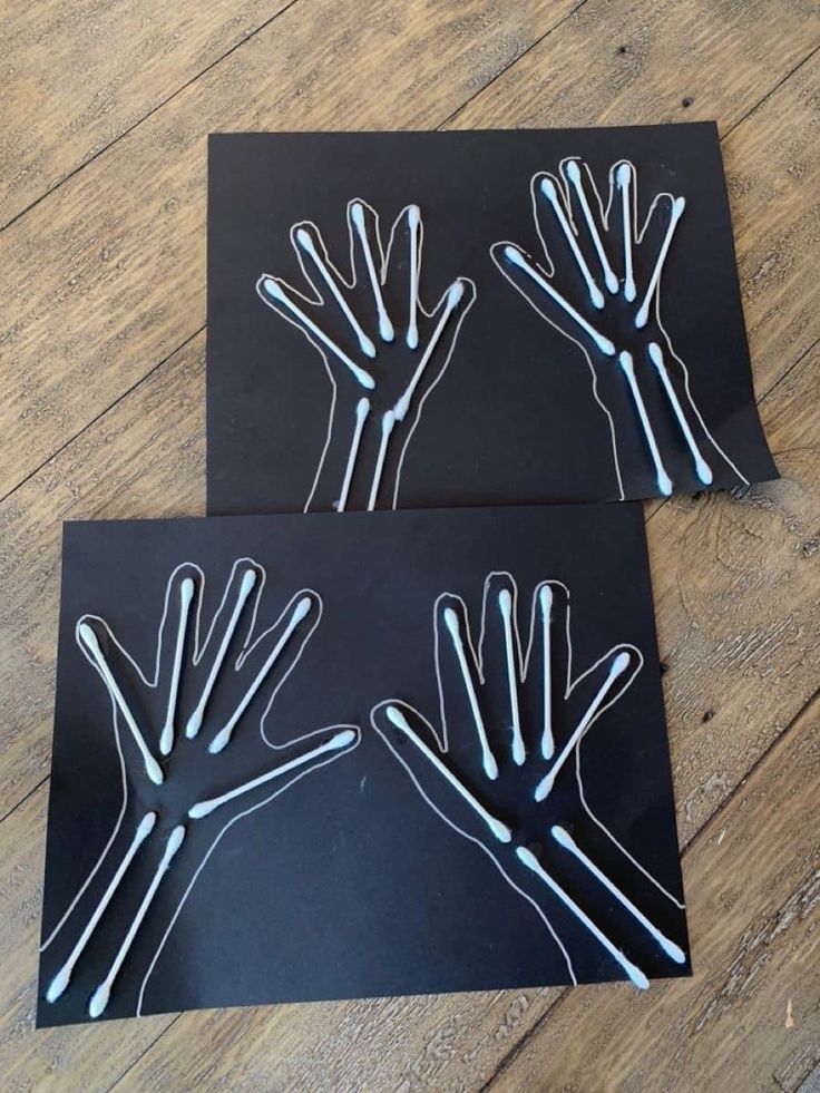 two pieces of black paper with white hand prints on them