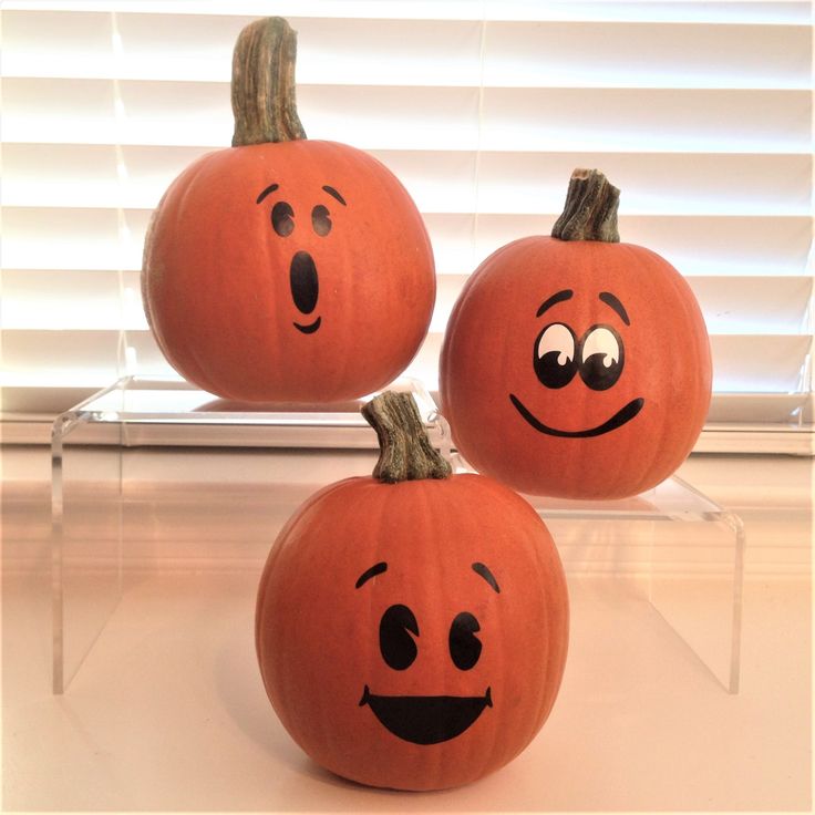 three pumpkins with faces drawn on them sitting in front of a window sill