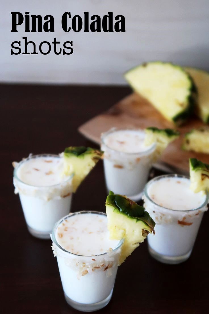 small glasses filled with pineapple shots sitting on a wooden table next to slices of pineapple