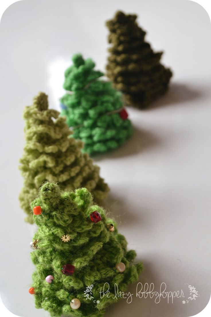 three crocheted christmas trees sitting on top of a white table next to each other