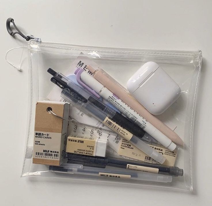 various pens and pencils in a clear plastic bag on a white surface with an airplug