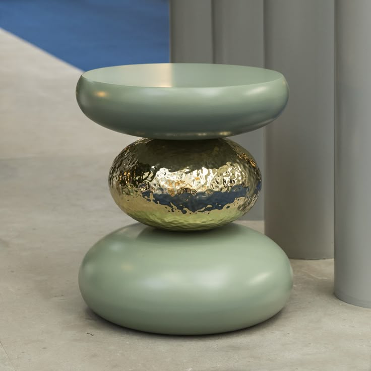 two green and gold vases sitting on top of each other next to metal poles