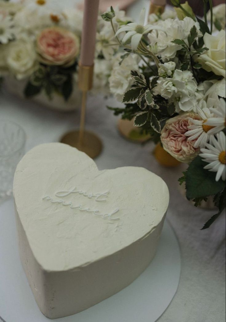 a white heart shaped cake sitting on top of a table next to flowers and candles