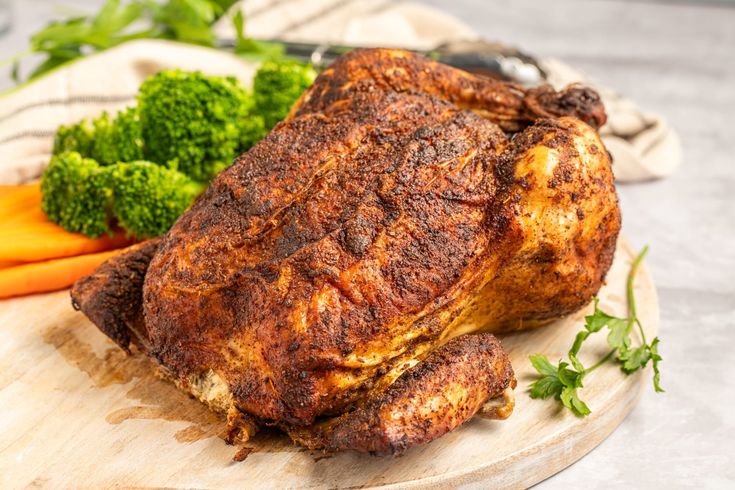 a whole chicken sitting on top of a wooden cutting board next to carrots and broccoli