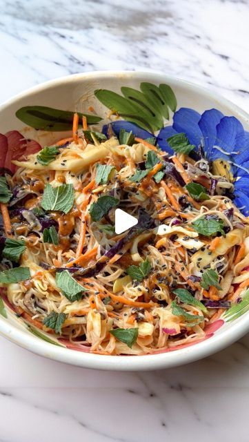 a bowl filled with noodles and vegetables on top of a marble countertop next to a fork