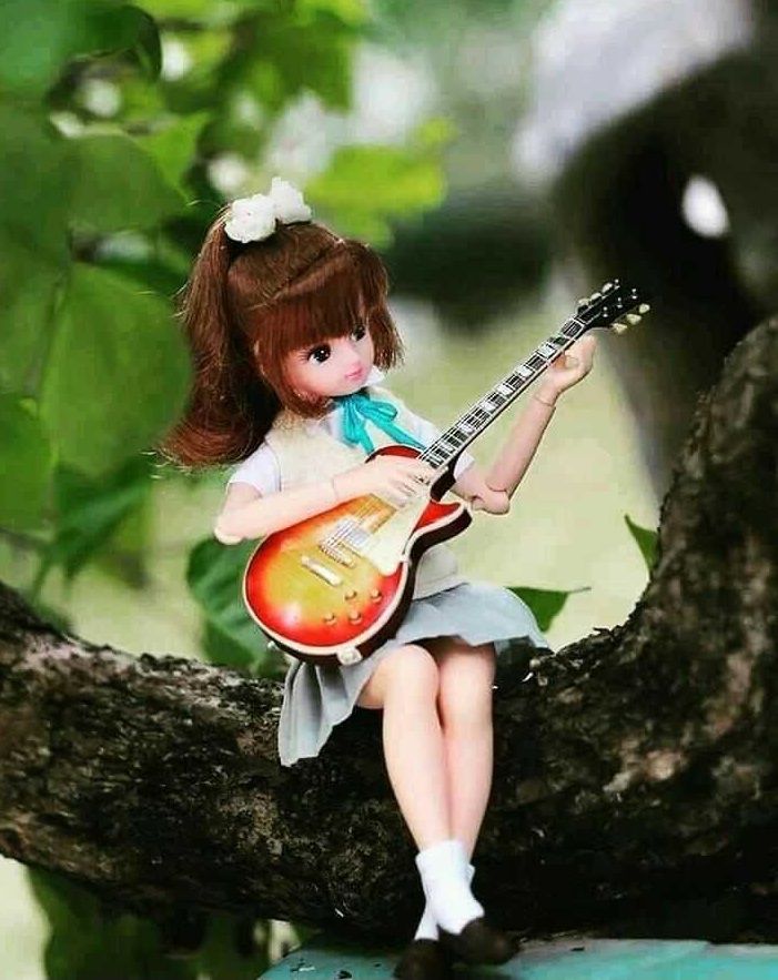 a doll is sitting on a tree branch with a guitar in her hand and holding it