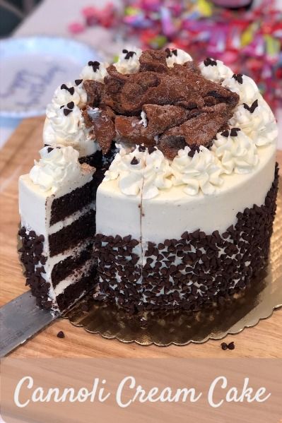 a cake with white frosting and chocolate toppings on a cutting board next to a knife