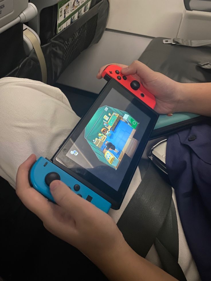 a person holding a nintendo wii game controller in their hand while sitting on an airplane