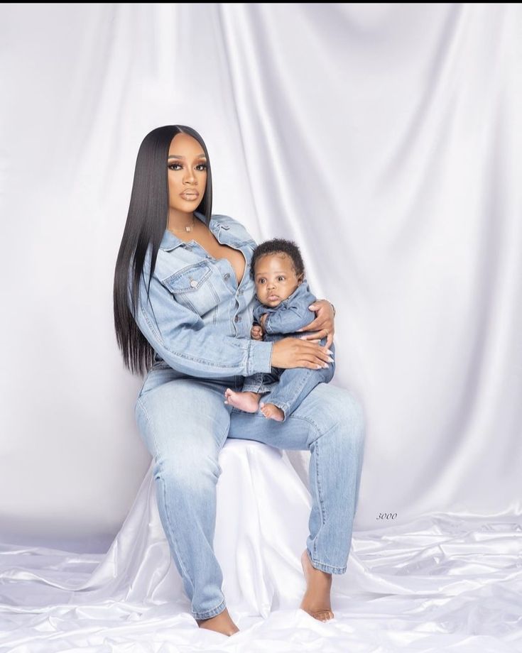 a woman holding a baby in her lap while sitting on top of a white sheet