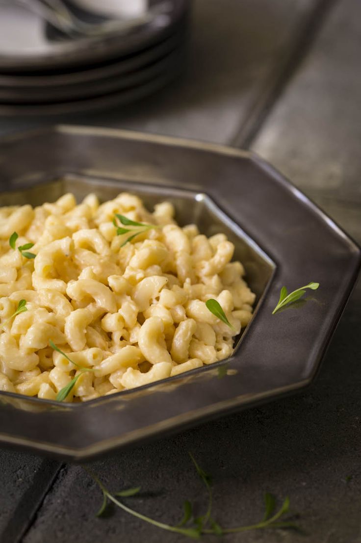 macaroni and cheese in a metal bowl on a table with plates behind it