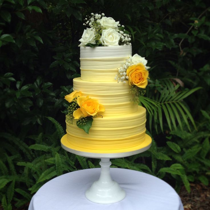 a yellow and white wedding cake sitting on top of a table in front of some bushes