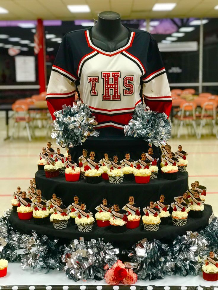 a table topped with cupcakes covered in frosting and cheerleader shirts on top of it