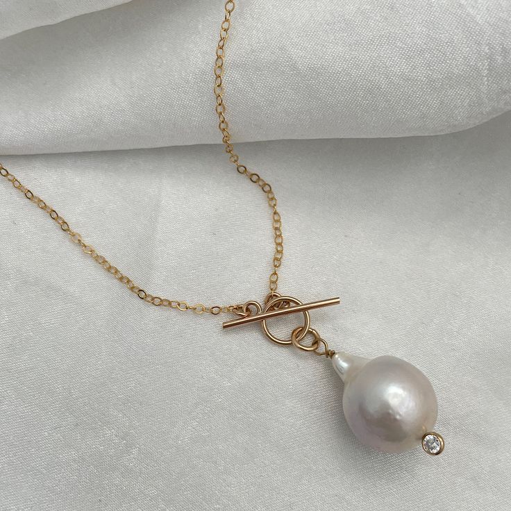 An unparalleled ocean treasure to call your own. A modern and sophisticated update on the classic pearl necklace. This stunner is perfect for creating today's ever-popular layered looks. A gorgeous freshwater 17mm to 21mm baroque pearl is worn on a toggle-style necklace and accented with cubic zirconia. Available in 14kt gold fill or sterling silver. Model wears a Big Baroque Pearl Necklace at 16 inches and one at 20 inches. genuine baroque pearl measuring 17mm to 21mm toggle style clasp 1.6mm cable chain 14kt gold fill or sterling silver cubic zirconia accent Shell Charm Necklace, Classic Pearl Necklace, Silver Model, Bee Studs, Silver Pearl Necklace, Baroque Pearl Necklace, Seashell Necklace, Gold Pearl Necklace, Cowrie Shell