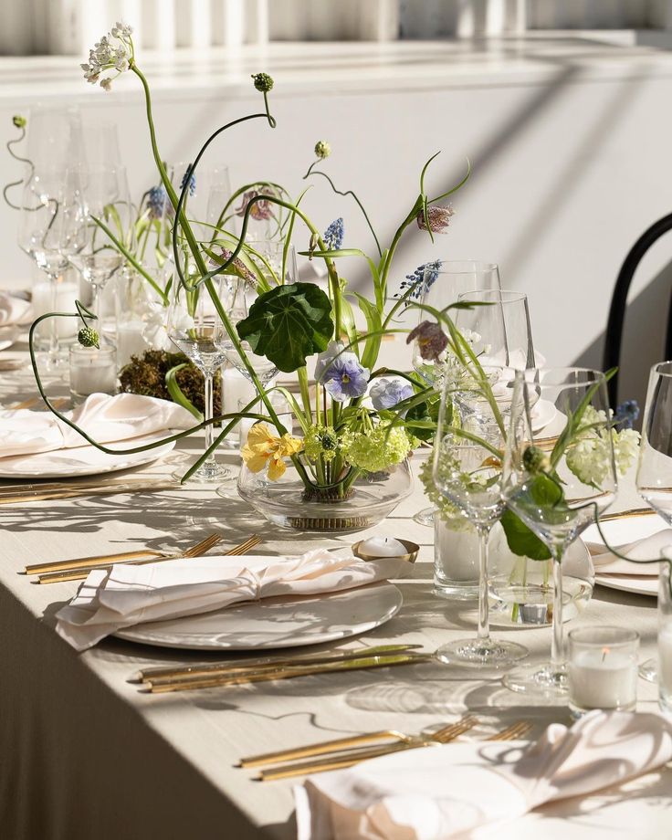 the table is set with white plates, silverware and flowers in glass vases