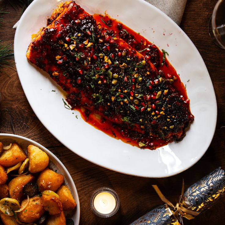 a white plate topped with meat covered in sauce next to potatoes and other food items