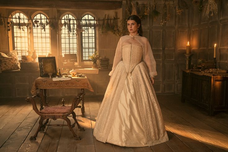 a woman in a white dress standing next to a table and chair with candles on it