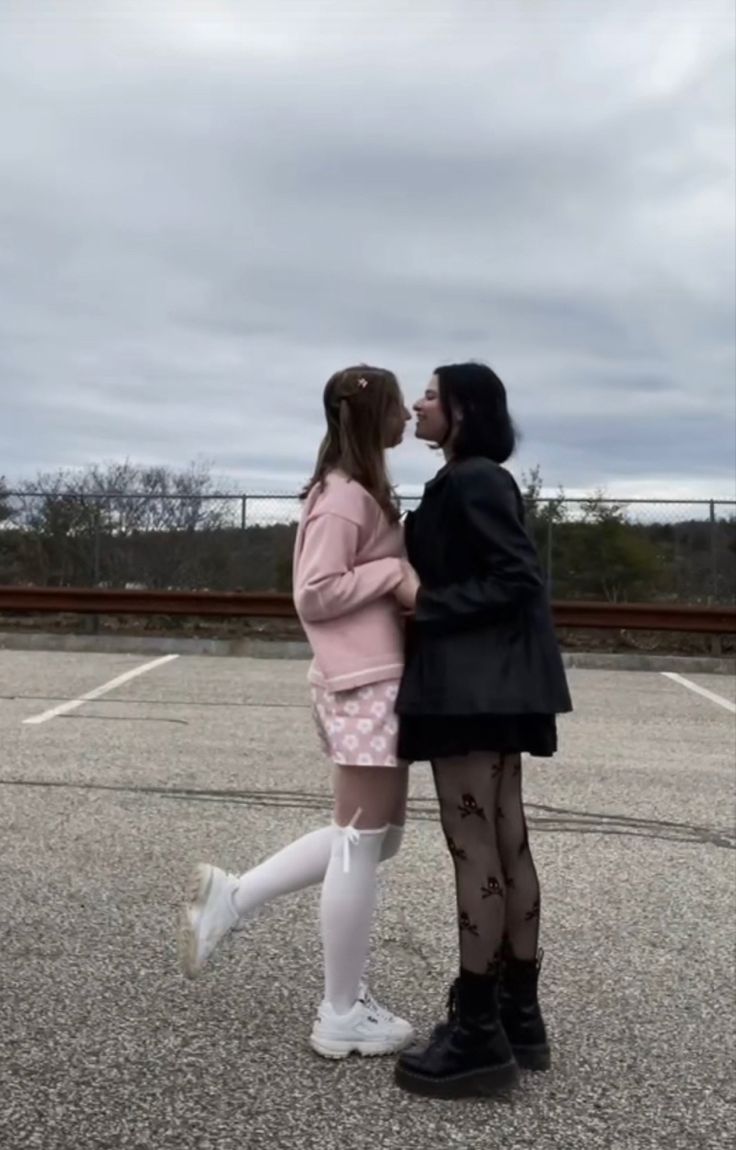 two people standing next to each other in an empty parking lot with one holding the other's hand