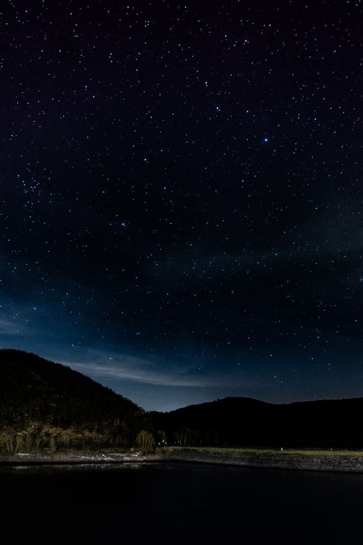 the night sky is filled with stars above a body of water and mountains in the distance