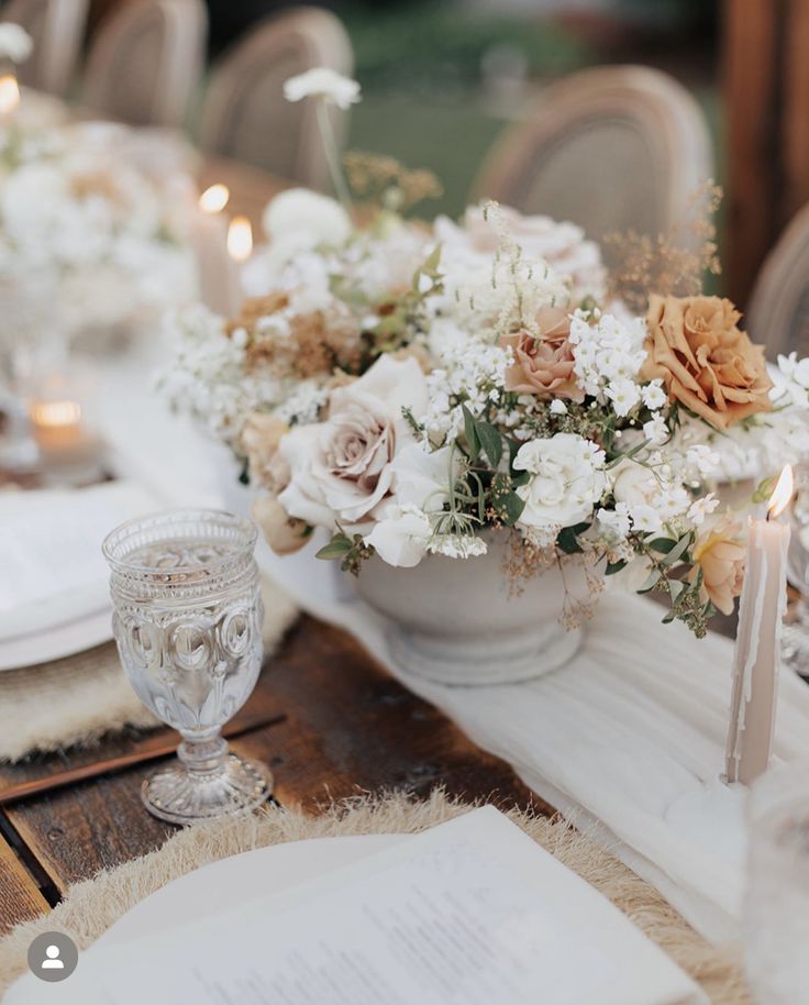 the table is set with white and peach flowers in vases, napkins, and candles